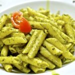 Pasta al pesto servita in un piatto, decorata con pinoli e basilico fresco.