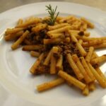 Pasta al ragù bianco servita in un piatto decorato, con erbe fresche e un tocco di formaggio grattugiato.