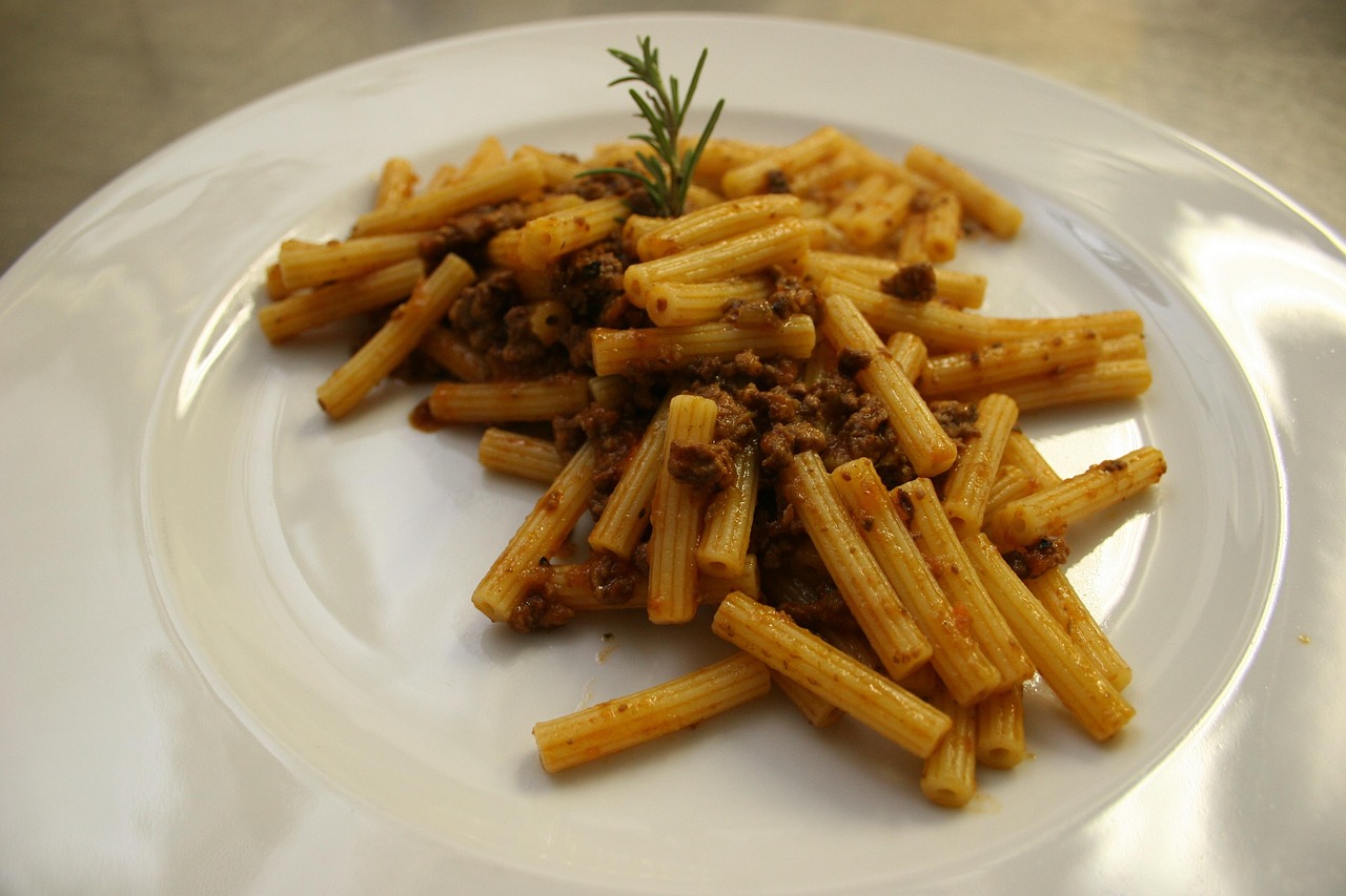 Pasta al ragù bianco servita in un piatto decorato, con erbe fresche e un tocco di formaggio grattugiato.