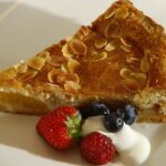 Crostata con base dorata, farcita con marmellata, su un piatto decorativo.