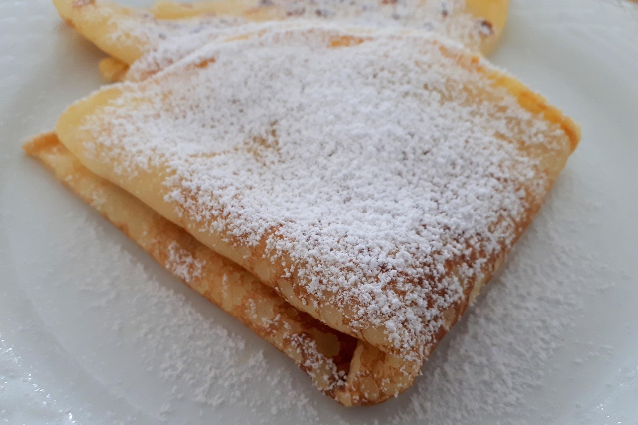 Crepes dolci appena cotte su un piatto, guarnite con zucchero a velo e frutta fresca.