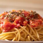 Spaghetti al tonno con pomodorini freschi, impiattati con gusto e colori vivaci.